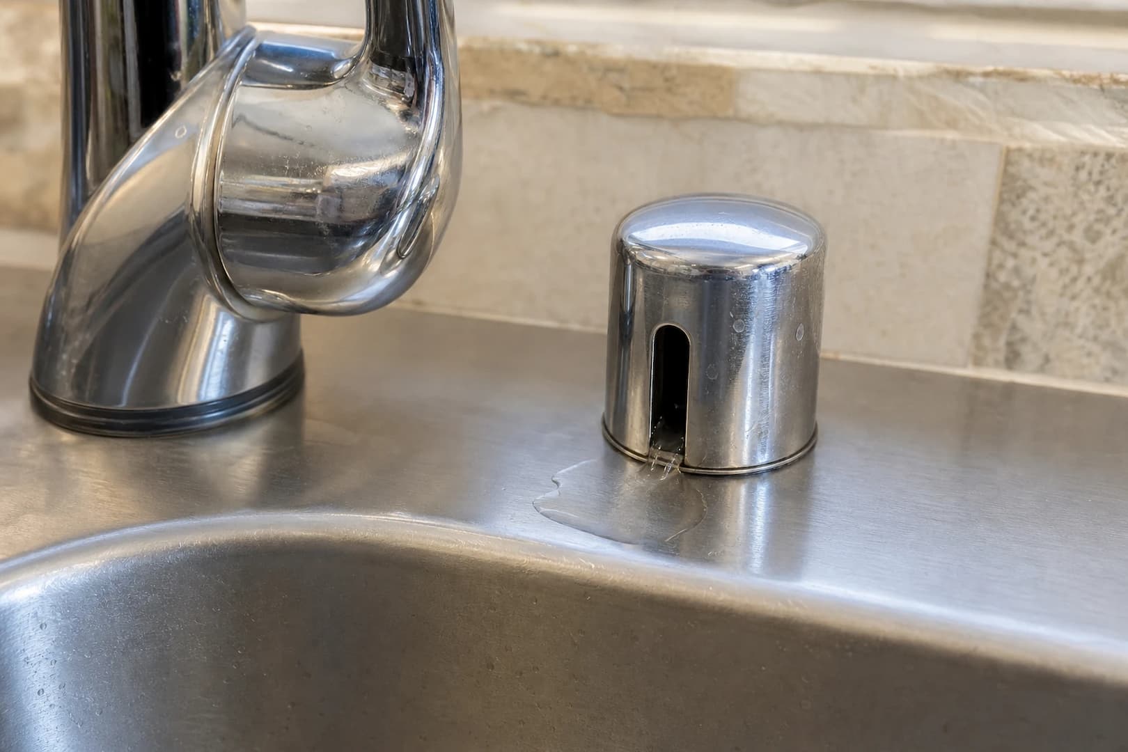 Small amount of water spilling from the side vent of a chrome dishwasher air gap