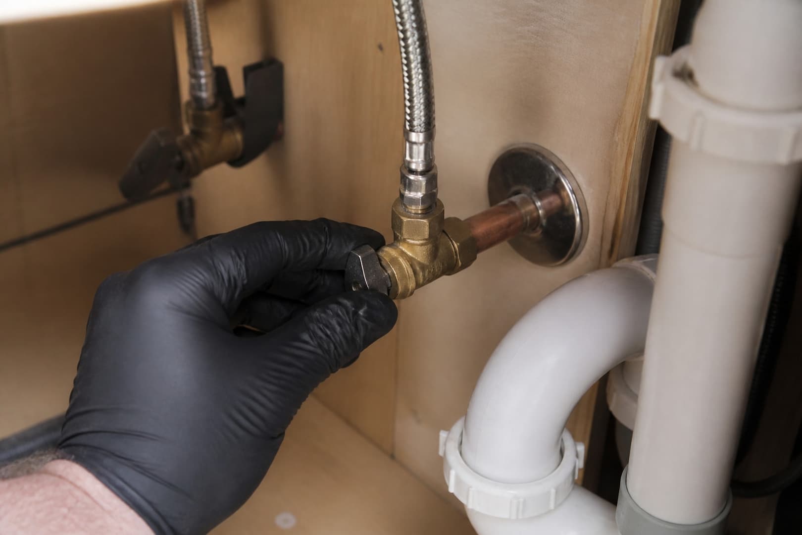 Gloved hand testing a brass quarter-turn angle stop under a sink