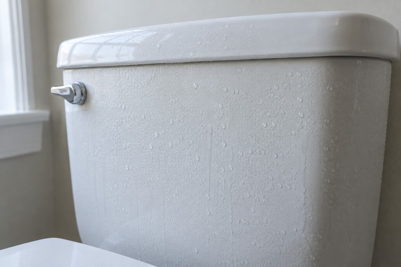 Small condensation droplets on the outside of a white porcelain toilet tank