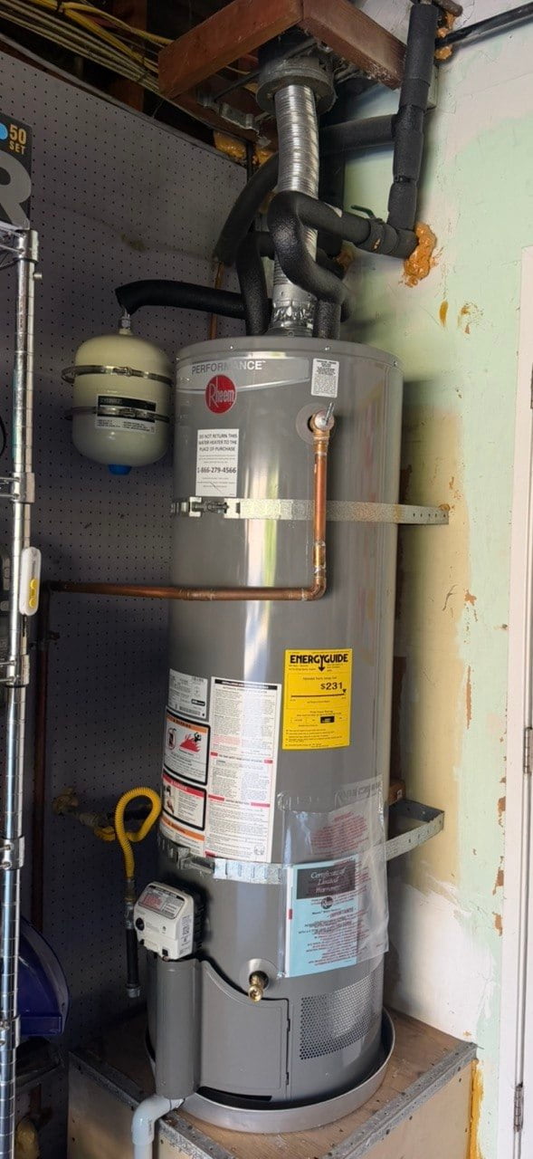 New gray Rheem gas water heater in the same utility space, with straps and insulated water piping