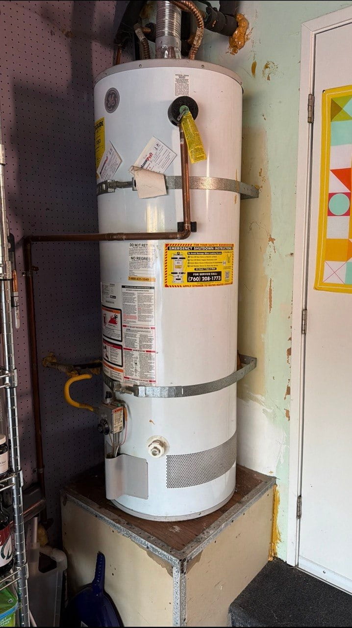 Older white GE gas water heater on a raised platform before replacement